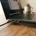 A close-up, low angle of meticulously organized USB-C cables neatly connected to a modern laptop on a warm wooden desk